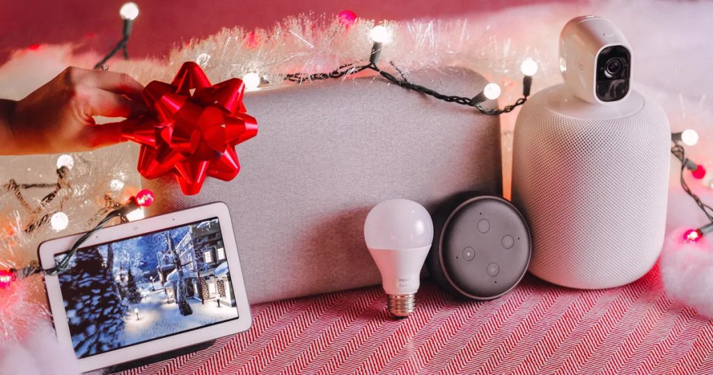 A picture of a 5 smart home devices, an Alexa Speaker, smart light bulb and others, with a bow and some lights